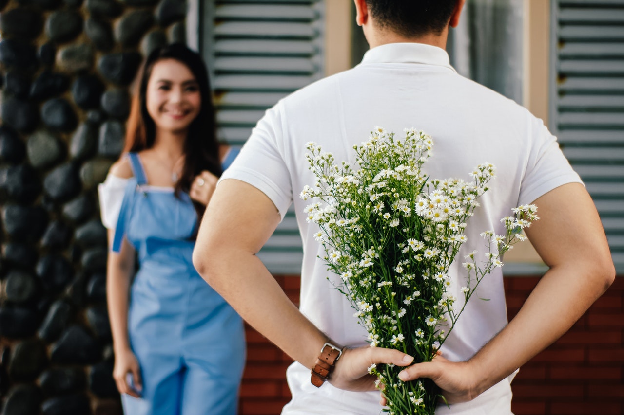 Man in white collared shirt surprised woman in denim jumpsuit with daisies