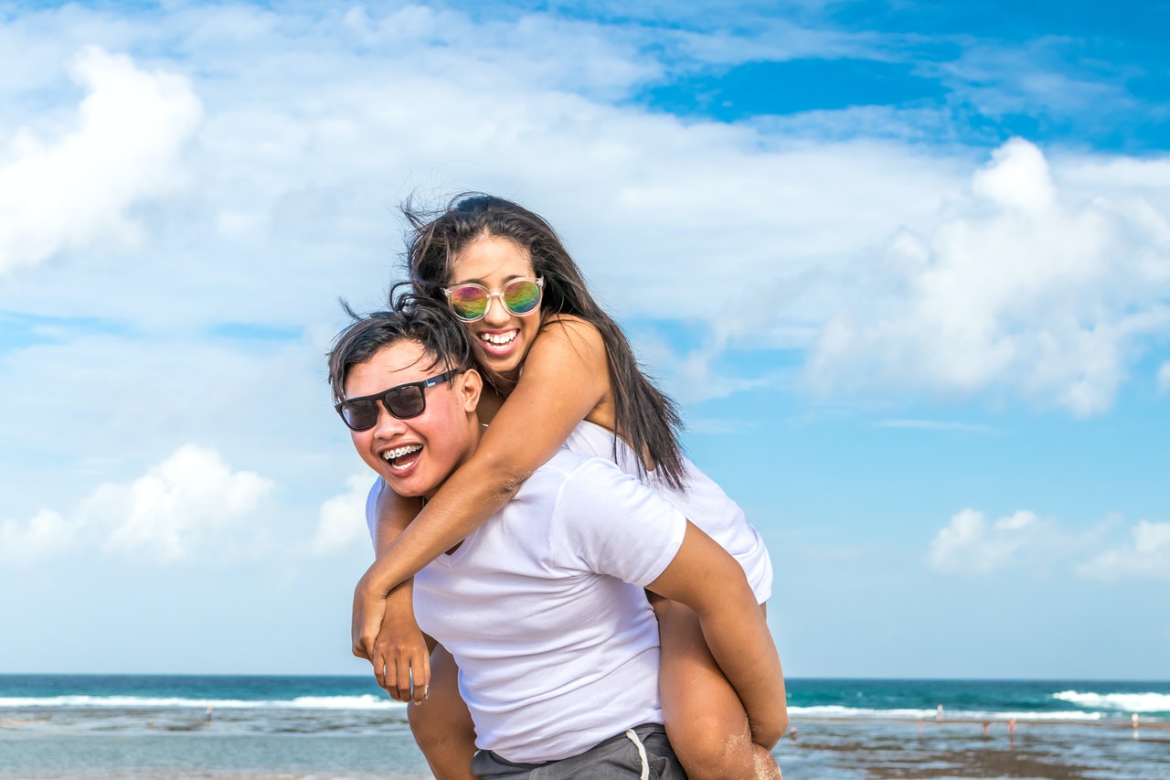 Man in white t-shirt carrying woman in white dress on his back