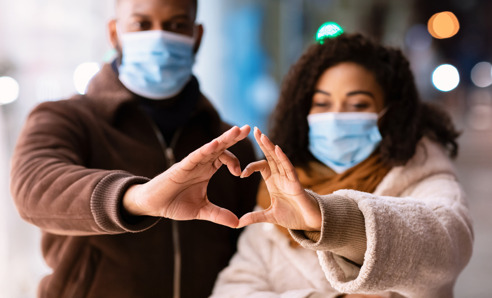 man and woman wearing medical masks making a heart figure with their hands