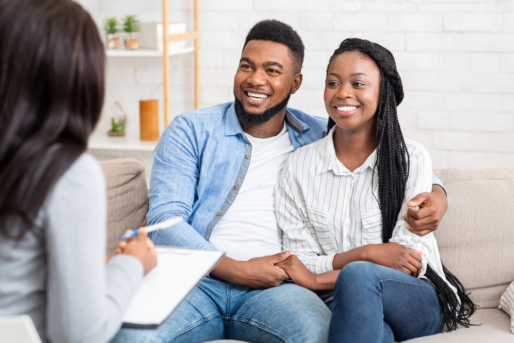 couple sitting on couch smiling while talking to therapist